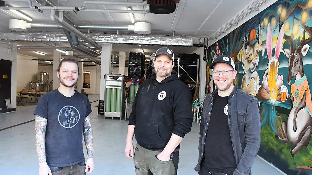 Tre medarbetare i Hyllie Bryggeris lokal i Malmö, med jäsningstankar och väggmålning.